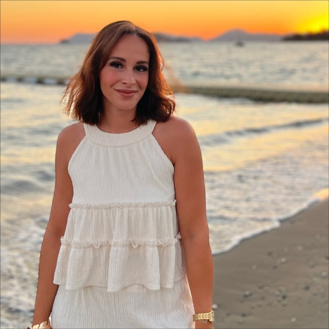 Smiling woman in white dress standing on a sunset beach.